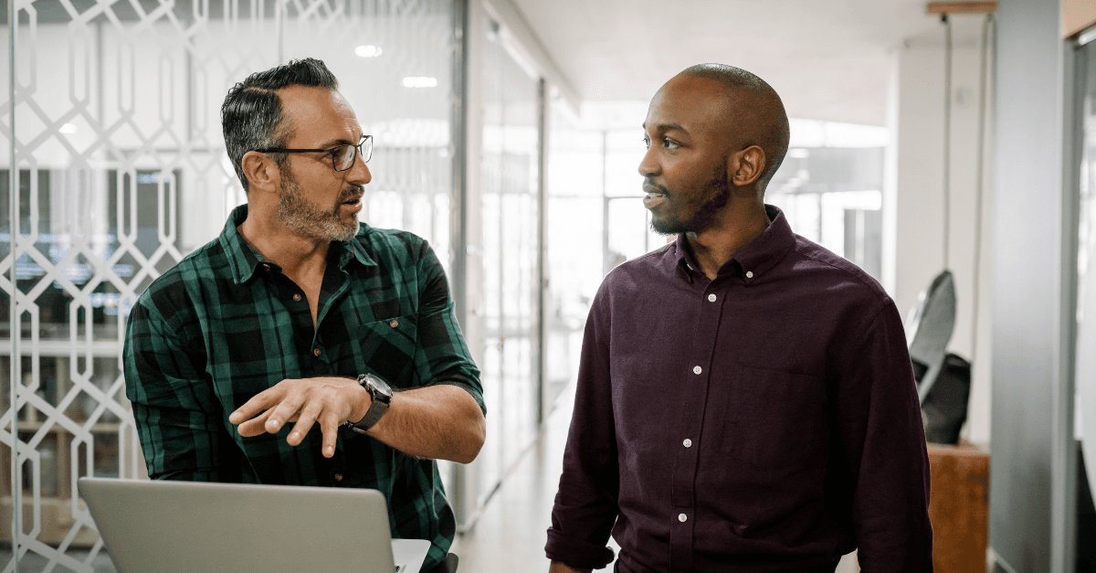 Two guys walking discussing content on laptop
